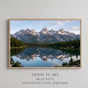 May include: A framed landscape print featuring a mountain range reflected in a calm lake. The image showcases snow-capped peaks, lush green trees, and a clear blue sky. The text at the bottom reads "FRAME TV ART, 4K QUALITY, HIGH RESOLUTION 3840X2160."