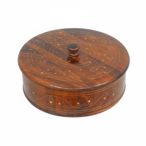 May include: A circular wooden box with a lid, showcasing a deep brown hue and decorative inlaid patterns. The lid is topped with a small, round knob. The sides and lid are adorned with detailed designs, highlighting its craftsmanship.