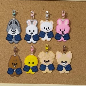 May include: Eight pixel art keychains featuring cartoon animal characters, each wearing a dark blue cape. The characters include a gray wolf, white rabbit, white bear, pink rabbit, brown bear, yellow chick, tan bear, and a light tan fox, all with metal clips.