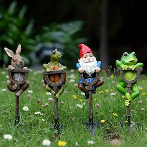 Könnte beinhalten: Gartenstecker-Set mit Tier- und Zwergfiguren. Die Stecker zeigen ein Kaninchen, eine Schildkröte, einen Zwerg und einen Frosch, die jeweils ein schaufelförmiges Schild halten. Die Figuren sind in natürlichen Farben bemalt.