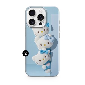May include: A clear smartphone case featuring a vertical stack of three white Hello Kitty plush figures against a light blue background. Each figure has a yellow nose, black eyes, and whiskers. The top figure has a blue bow, and the others wear blue.