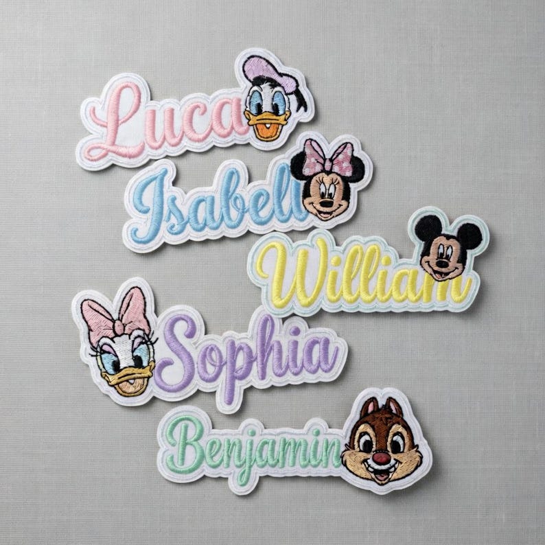 May include: Embroidered name patches featuring Disney characters like Mickey Mouse, Minnie Mouse, Donald Duck, and Daisy Duck. Each patch has a different name in a cursive font, with a white border. Names include Luca, Isabel, William, Sophia, and Benjamin.