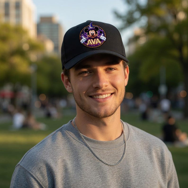 May include: Black baseball cap with a circular patch featuring Mickey Mouse in a wizard hat, the name "AVA", and purple and gold accents. The cap is worn by a person.