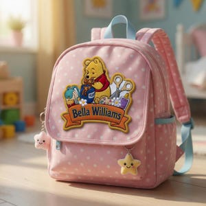 Op de afbeelding: Roze rugzak met witte stippen met een Winnie de Poeh-patch en de naam "Bella Williams". De rugzak heeft lichtblauwe bandjes en ster-vormige sleutelhangers. Een charmant en praktisch accessoire voor kinderen.