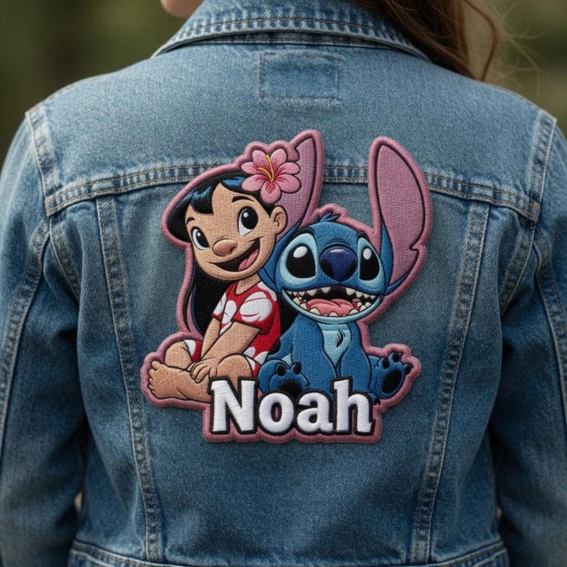 May include: A light blue denim jacket featuring a large embroidered patch on the back. The patch depicts a cartoon girl with a pink flower in her hair and a blue alien character, with the name Noah printed in white letters below them.