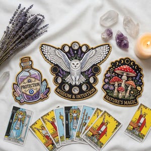 May include: Three embroidered patches featuring a white owl with the text Wisdom & Intuition, a potion bottle labeled Protection, and mushrooms with the text Nature's Magic, arranged above several tarot cards including The High Priestess and The Magician.