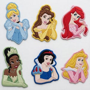 May include: Embroidered patches featuring six different princess designs. Each patch showcases a princess with detailed facial features, hair, and attire. The princesses are depicted in various colors, including blue, yellow, red, pink, green, and white.
