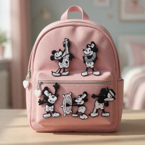 Op de afbeelding: Een roze rugzak met meerdere zwart-witte Mickey Mouse-personagepatches. De rugzak heeft een voorvak, een handvat aan de bovenkant en hartvormige ritstrekkers. De patches tonen Mickey Mouse in verschillende poses.