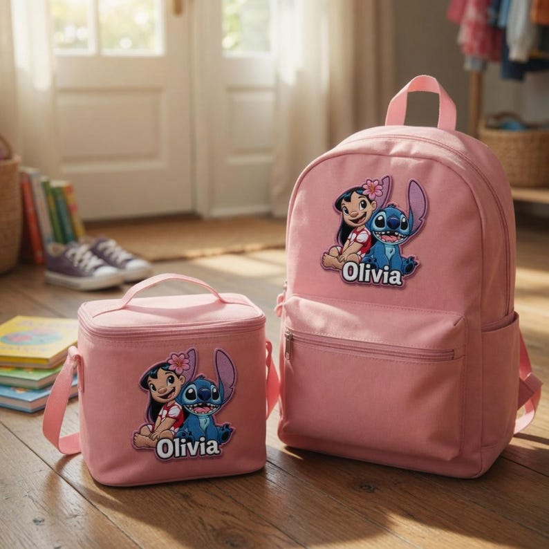 May include: A pink backpack and a matching lunch bag, both featuring a graphic of Lilo and Stitch with the name Olivia printed below. The items have a top handle, a front zippered pocket, and a smooth fabric construction in a soft pink shade.