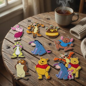 May include: A collection of embroidered patches featuring Winnie the Pooh characters including Piglet, Tigger, Eeyore, Roo, Owl, and a honey pot with bees. The patches are arranged on a wooden surface next to a steaming mug and a knit fabric.