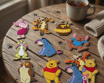 May include: A collection of embroidered patches featuring Winnie the Pooh characters including Piglet, Tigger, Eeyore, Roo, Owl, and a honey pot with bees. The patches are arranged on a wooden surface next to a steaming mug and a knit fabric.