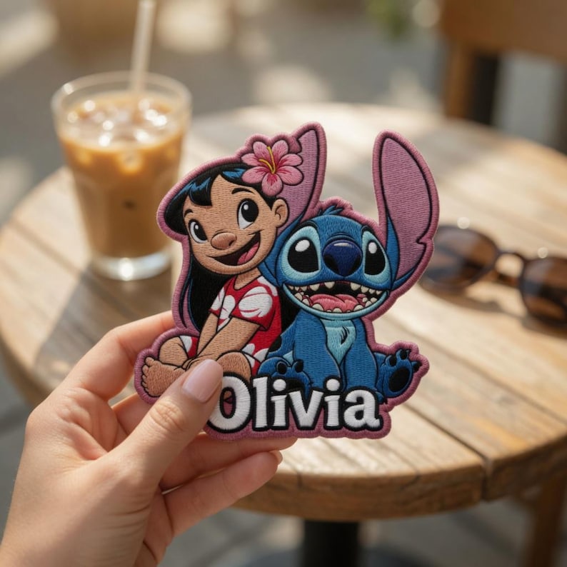May include: An embroidered patch featuring the characters Lilo and Stitch. Lilo has black hair with a pink flower, wearing a red and white patterned top. Stitch is blue with large ears. The name Olivia is embroidered in white at the bottom.