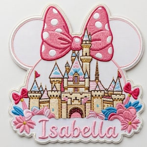 May include: An embroidered patch featuring a castle silhouette with a large pink and white polka dot bow at the top. The design includes blue and pink floral accents, small bows, and the name Isabella embroidered in pink script at the bottom.