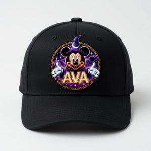 May include: Black baseball cap featuring a circular patch with Mickey Mouse dressed as a wizard. The patch includes the name "AVA" in gold lettering, a purple and gold border, and a starry background. The cap has a curved brim.