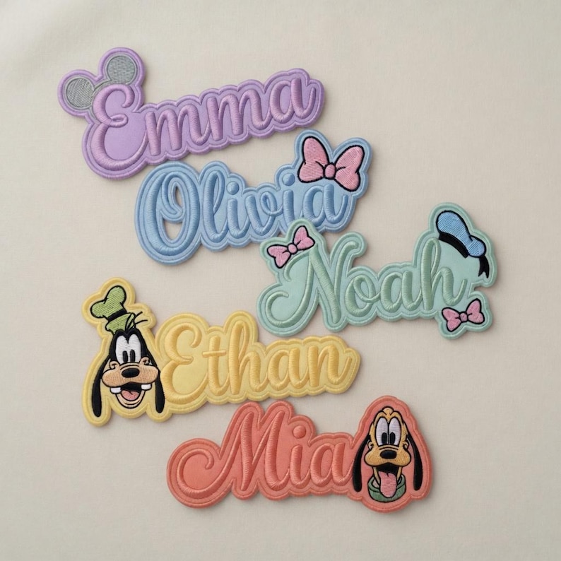 May include: Embroidered name patches in various colors, including lavender, blue, yellow, and coral. Each patch features a name in a cursive font, with Disney character accents like Minnie Mouse ears, bows, and character faces. Ideal for personalizing clothing or accessories.