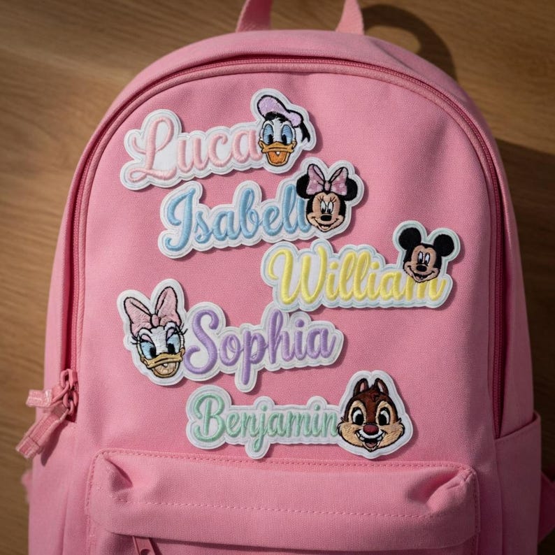 May include: Pink backpack with embroidered patches featuring Disney characters and names like "Luca," "Isabella," and "William." The patches include images of Donald Duck, Minnie Mouse, and Mickey Mouse. The backpack has a front pocket and a zipper closure.