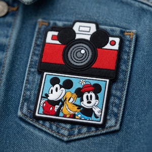 Puede incluir: Un bolsillo de chaqueta vaquera presenta un parche bordado colorido. El parche representa un dise&ntilde;o de c&aacute;mara roja y negra sobre una imagen rectangular de Mickey Mouse, Pluto y otro personaje de Mickey Mouse. El parche es un accesorio divertido.