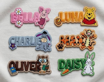 May include: Embroidered name patches featuring various characters and names. The patches include names like "BELLA", "LUNA", "CHARLIE", "MAX", "OLIVER", and "DAISY", each with a corresponding cartoon character such as Winnie the Pooh, Piglet, and Tigger. The patches are in various colors.