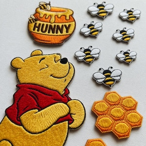 May include: Embroidered patches featuring Winnie the Pooh, a honey pot with the word "HUNNY", bees, and a honeycomb. The patches are yellow, red, black, and white, with detailed stitching. Ideal for decorating clothing or accessories.
