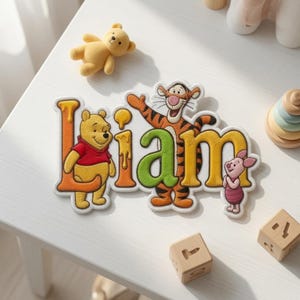May include: A decorative wall sign featuring the name LIAM in large, colorful, bubble-style letters. Winnie the Pooh stands by the letter L, Tigger is integrated into the letter A, and Piglet stands next to the letter M, all with honey accents.