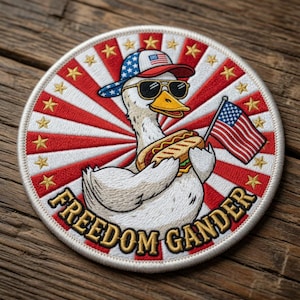 May include: Embroidered patch with a cartoon goose wearing sunglasses and a patriotic hat, holding a hot dog and an American flag. The patch has a red, white, and blue colour scheme with the words "FREEDOM GANDER" in gold.