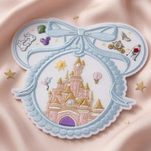May include: A white embroidered patch shaped like mouse ears with a light blue ribbon border. The center features a pink and gold castle, a yellow sun, and a hot air balloon. Smaller embroidered icons include a white rabbit, a glass slipper, a carriage, and a rose.