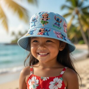 May include: A light blue bucket hat decorated with cartoon character designs. The hat has a wide brim and is worn by a young girl in a red floral dress. The background shows a beach with palm trees and blue water.