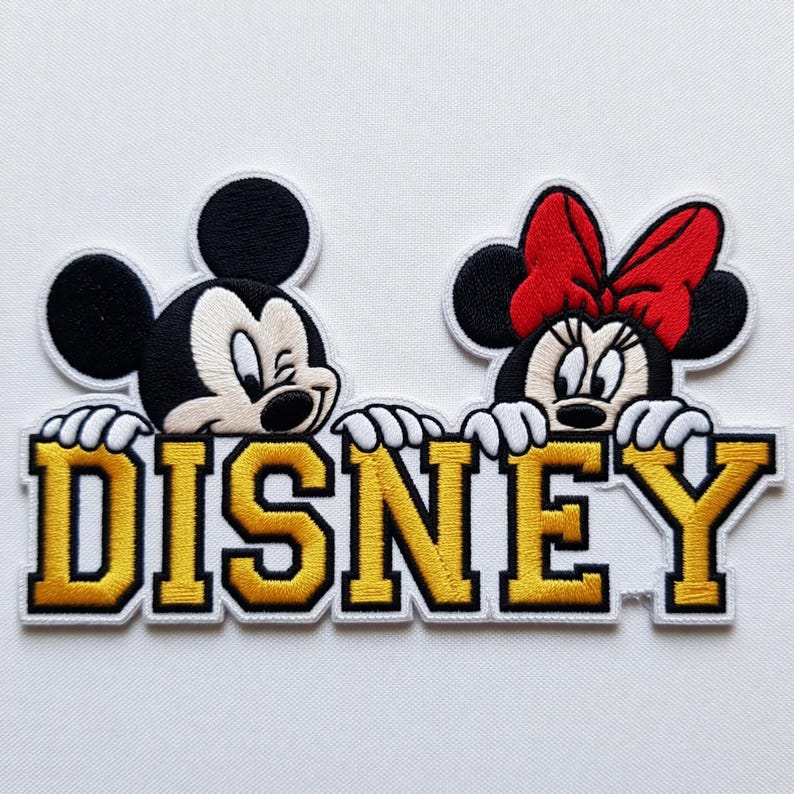 Puede incluir: Parche bordado con Mickey Mouse y Minnie Mouse sobre la palabra "DISNEY" en dorado y blanco. Mickey est&aacute; a la izquierda, Minnie a la derecha con un lazo rojo. El parche est&aacute; sobre un fondo blanco.