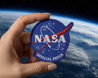 May include: A blue NASA Official Patch with white text and a red swoosh. The patch features the NASA logo and the words "OFFICIAL PATCH". The patch is held in front of a background of the Earth and space.