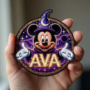 May include: Embroidered patch featuring Mickey Mouse in a wizard's hat and robe, with the name "AVA" in gold lettering. The patch has a purple and gold color scheme with a starry background, and a crescent moon on the hat.