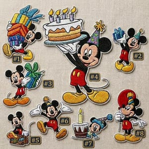May include: Embroidered patches featuring Mickey Mouse in various birthday-themed poses. Mickey is shown holding gifts, a cake with candles, and wearing a party hat. The patches are in red, black, yellow, and blue.