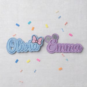 May include: Two embroidered name patches, "Olivia" in light blue with a pink bow, and "Emma" in purple with mouse ears. Colorful confetti is scattered around the patches on a white background.