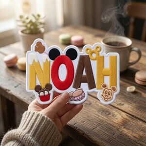 May include: A custom embroidered patch featuring the name NOAH in large, colorful letters. The letter O is designed with black mouse ears, and the patch includes decorative elements like a cupcake, a macaron, and a small mouse-shaped icon.