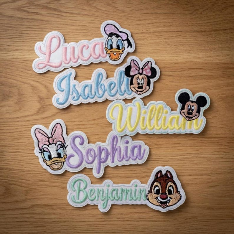 May include: Embroidered name patches featuring Disney characters. Names include Luca, Isabel, William, Sophia, and Benjamin, each with a corresponding character like Donald Duck, Minnie Mouse, Mickey Mouse, Daisy Duck, and Chip. The patches have a white border and colorful lettering.