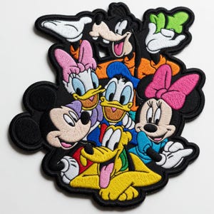 Op de afbeelding: Een geborduurde patch met een groep stripfiguren, waaronder Mickey Mouse, Minnie Mouse, Donald Duck, Daisy Duck, Goofy en Pluto. De figuren zijn in een groep gerangschikt met levendige kleuren en een dikke zwarte geborduurde rand.
