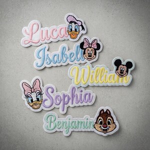 May include: Embroidered patches featuring names like Luca, Isabel, William, Sophia, and Benjamin, each with a Disney character design. The patches have a white border and are in various pastel colors.