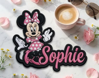 May include: An embroidered patch featuring the cartoon character Minnie Mouse wearing a pink polka-dot dress and bow, positioned next to the name Sophie written in a pink cursive font with a thick black outline on a white fabric backing.