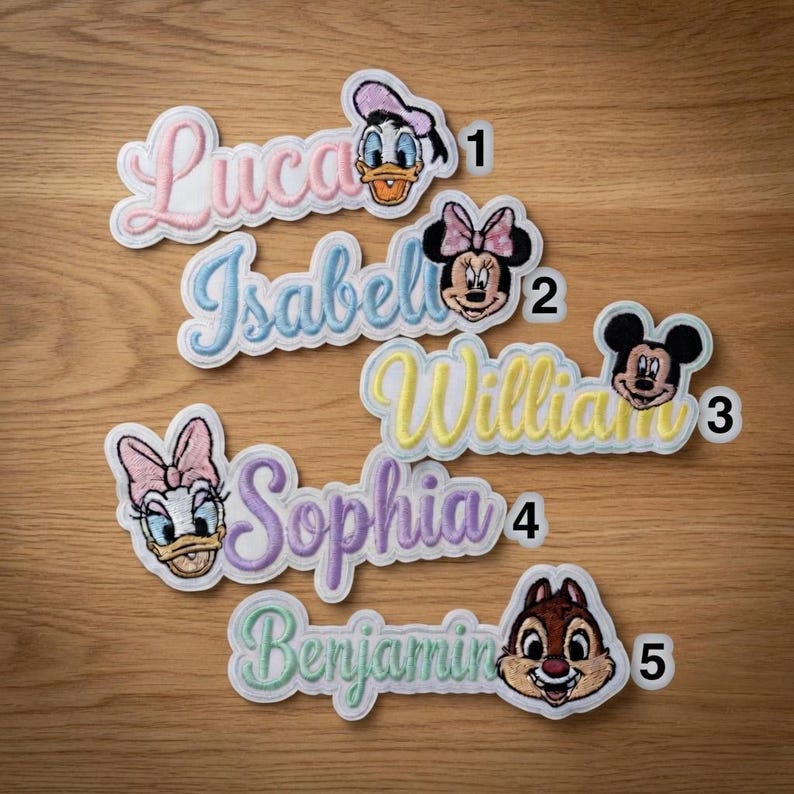 May include: Embroidered name patches featuring Disney characters. The patches include names like Lucas, Isabel, William, Sophia, and Benjamin, each with a corresponding character such as Donald Duck, Minnie Mouse, and Mickey Mouse. The patches have a white border and are in various pastel colors.