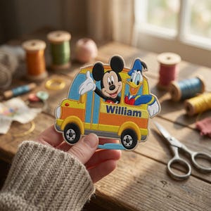 Op de afbeelding: Een geborduurde patch met Mickey Mouse en Donald Duck in een gele schoolbus. De bus heeft blauwe accenten en de naam William is in blauwe letters aan de zijkant geborduurd. De patch heeft een witte rand en gedetailleerd stikwerk.