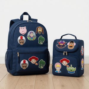 May include: A navy blue backpack and a matching navy blue lunch bag, both featuring various embroidered patches of animated characters from the Toy Story film series, including Buzz Lightyear, Woody, Jessie, Rex, Hamm, Slinky Dog, and Mr. Potato Head.
