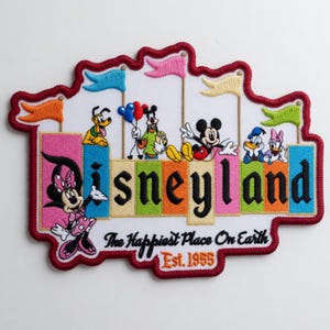 May include: Embroidered Disneyland patch featuring Mickey Mouse, Minnie Mouse, Pluto, Donald Duck, and Daisy Duck. The patch has a red border and includes the text "Disneyland", "The Happiest Place On Earth", and "Est. 1955".