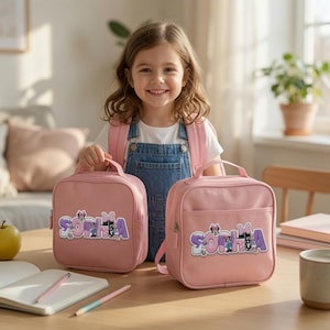 May include: Two matching light pink square lunch bags featuring the name SOPHIA in large, purple and white bubble letters with small Minnie Mouse character graphics integrated into the text. Each bag has a top handle and a front pocket.