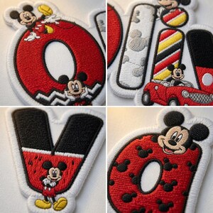 May include: A collection of four embroidered patches featuring the letters O, L, I, V, and D. Each letter incorporates Mickey Mouse imagery, including a red car, black and white patterns, and small mouse head silhouettes in red and black thread.