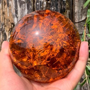 May include: A spherical object made of translucent amber-colored glass with a cracked, internal texture. The surface is smooth and polished, reflecting light across its multifaceted interior, creating a deep, warm orange glow throughout the sphere.
