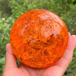 May include: A spherical object made of translucent orange glass with a cracked, internal texture. The surface is smooth and polished, while the interior displays a complex network of fractures that catch the light, creating a vibrant, glowing effect.