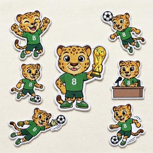 May include: A collection of seven embroidered patches featuring a cartoon leopard character wearing a green jersey with the number 8. The leopard is depicted in various soccer-themed poses, including holding a gold trophy, kicking a ball, and sitting at a desk with a microphone.