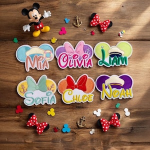 May include: A selection of personalised Disney-themed name patches and accessories. The patches feature names such as Mia, Olivia, and Liam, with Mickey Mouse ears and bows. A Mickey Mouse figurine and polka-dot bows are also present.