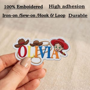 May include: An embroidered patch featuring the name OLIVIA in colorful letters, two brown cowboy hats, a lasso, and a red-haired character wearing a red hat. Text above reads 100% Emboidered, High adhesion, Iron-on /Sew-on /Hook & Loop, Durable.