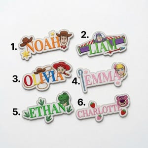 May include: Six embroidered fabric patches featuring character themes and names. Patch 1: NOAH with Woody. Patch 2: LIAM with Buzz Lightyear. Patch 3: OLIVIA with Jessie and a lasso. Patch 4: EMMA with Bo Peep and a staff. Patch 5: ETHAN with Rex. Patch 6: CHARLOTTE with Lotso and strawberries.
