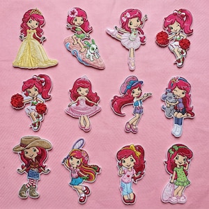 May include: A collection of colorful embroidered patches featuring a cartoon girl with pink hair. The patches depict the girl in various outfits and poses, including a ballerina, cheerleader, and cowgirl. The patches are on a pink background.